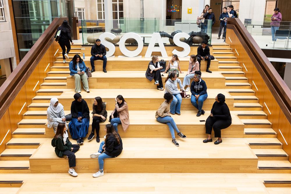 Students sitting in atrium next to SOAS letters