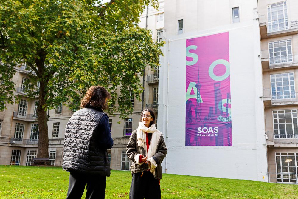 Two students chatting outside in front of SOAS banner