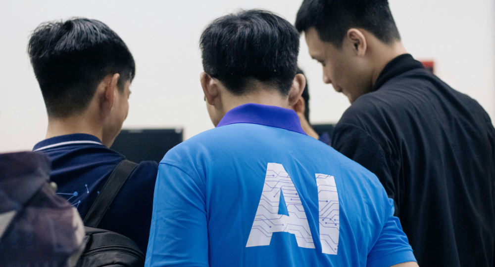 Group of men talking with one in blue tshirt with AI written on the back