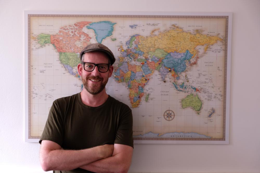 Benjamin Worku-Dix, founder of PositiveNegatives, pictured in front of a coloured map of the world.