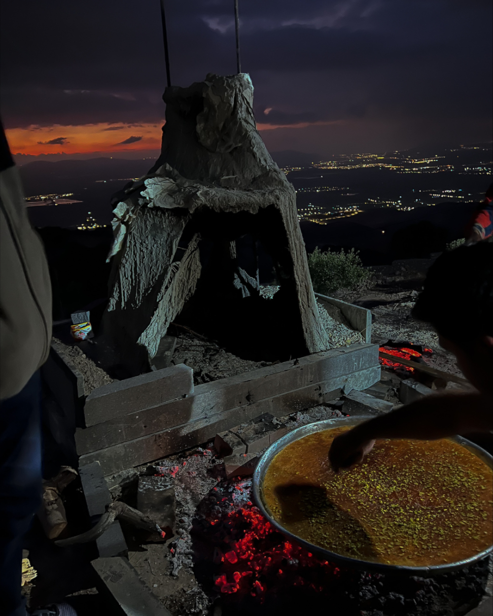 A person cooks Palestinian Knafeh in a big pot, with views of occupied West Bank in the background. 