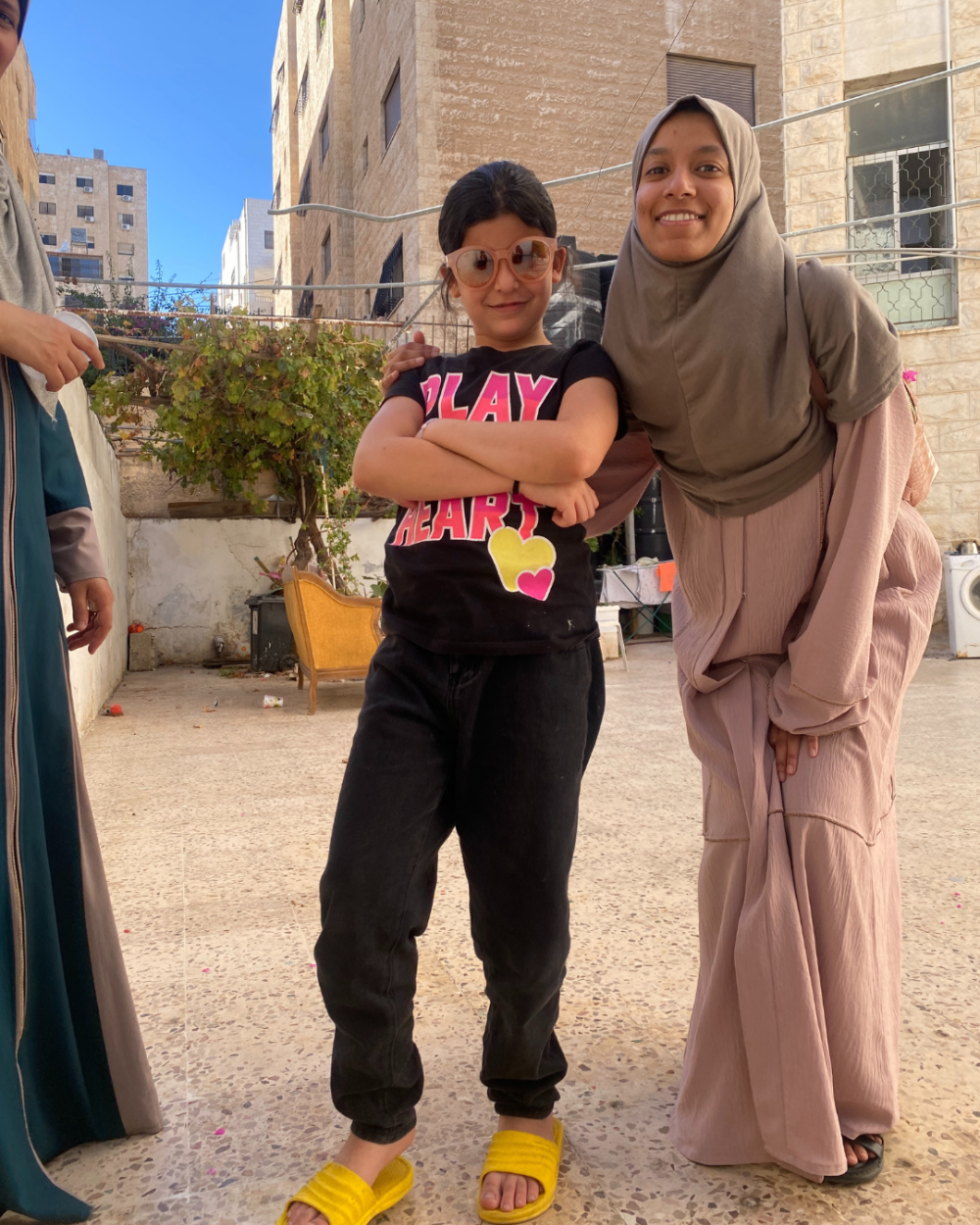 A child and a university student pose and smile in a courtyard. 